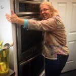 Lizzie is pictured hugging an oven. Caffè Lena's baker has blonde hair, glasses, and is wearing a colorful top.